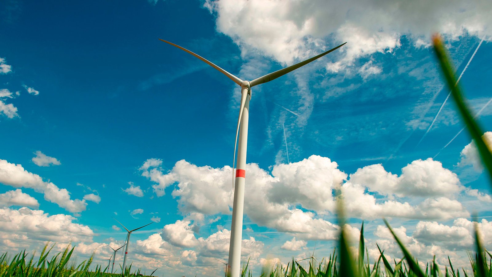 Wind turbine in the foreground of a green field in Villers-le-Bouillet, near Liège (Belgium), under a blue sky with clouds, with more wind turbines visible on the horizon. Energy