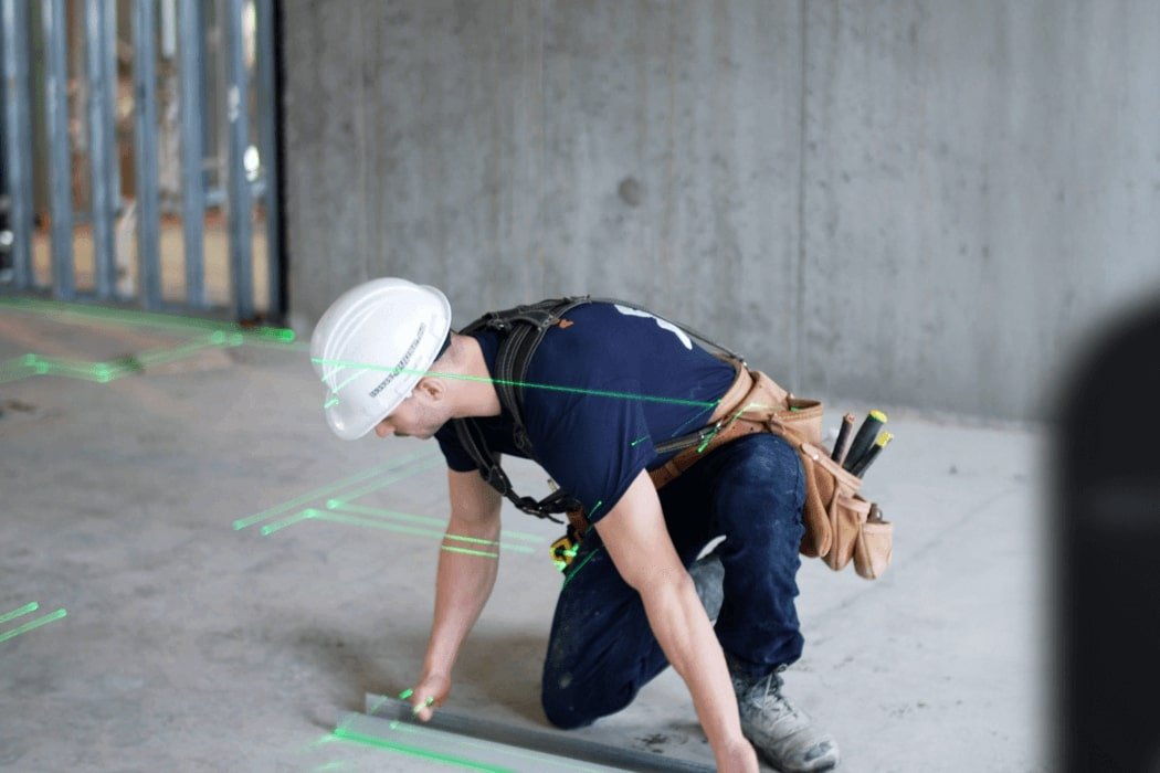 Construction worker kneels on floor with lasers