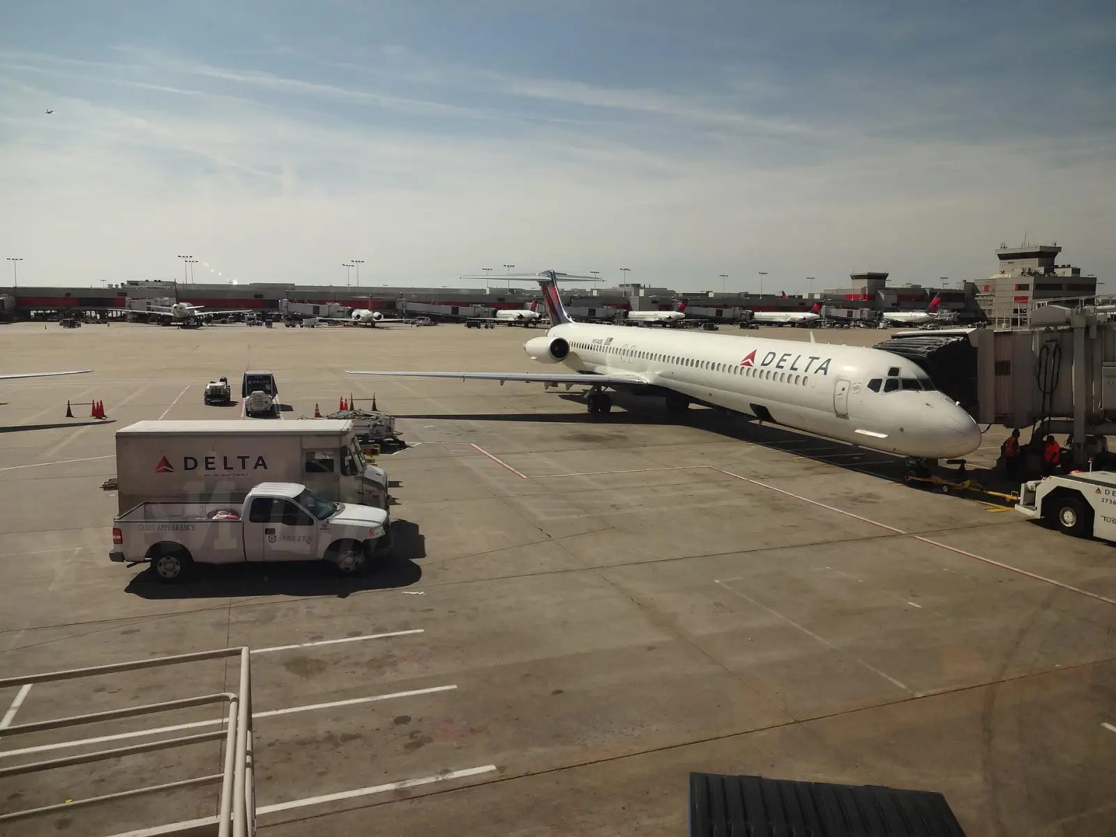 Delta A330 at airport gate with service vehicles on tarmac, ahead of boarding.