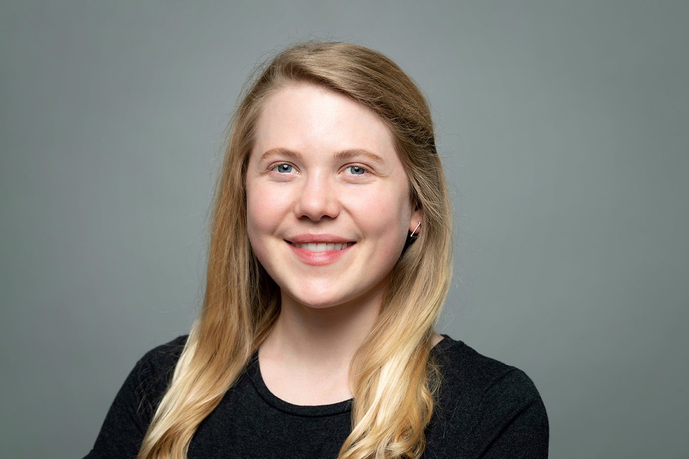 Claire Beskin, a young white woman with blonde hair, smiling against a gray backdrop.