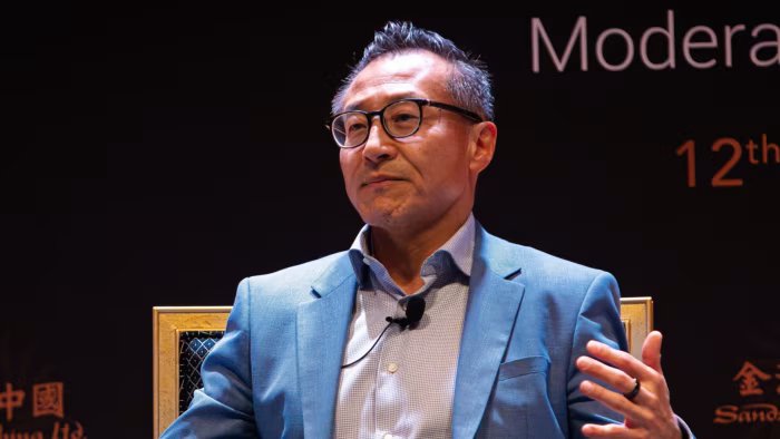 Joseph Tsai speaks during a sports ownership event, wearing a blue jacket and glasses.
