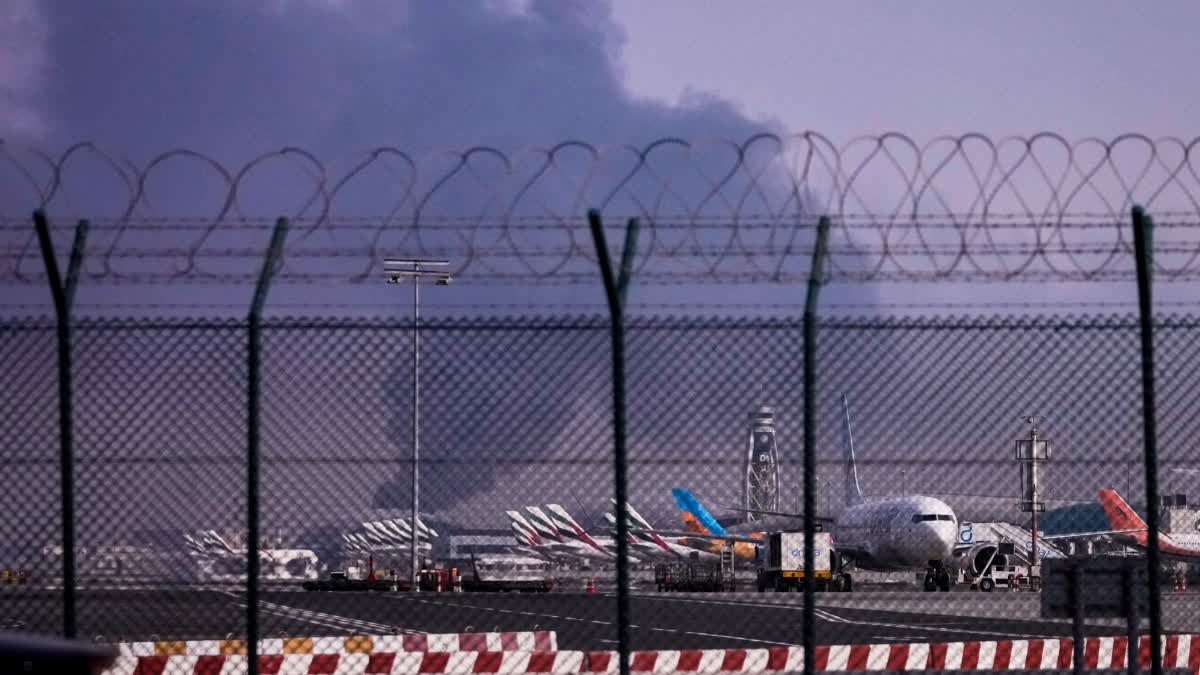 Planes are parked at Dubai International Airport as smoke rises in the background after a drone struck a fuel tank early morning, forcing the temporary suspension of flights, in Dubai, United Arab Emirates, Monday, March 16, 2026.