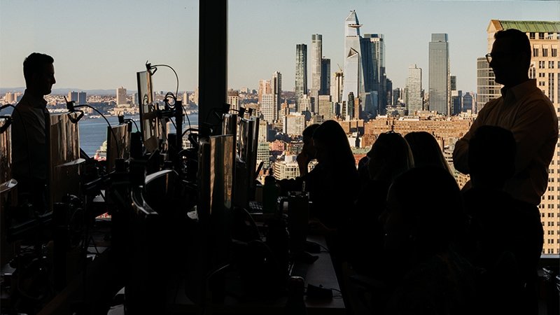 People cast n shadow gathered around computers