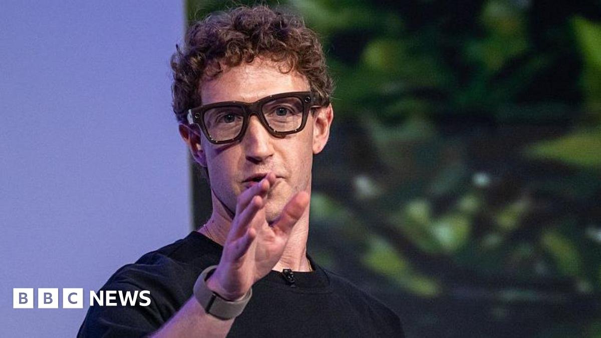 Mark Zuckerberg wearing thick black rimmed smart glasses and gesturing with his hand.