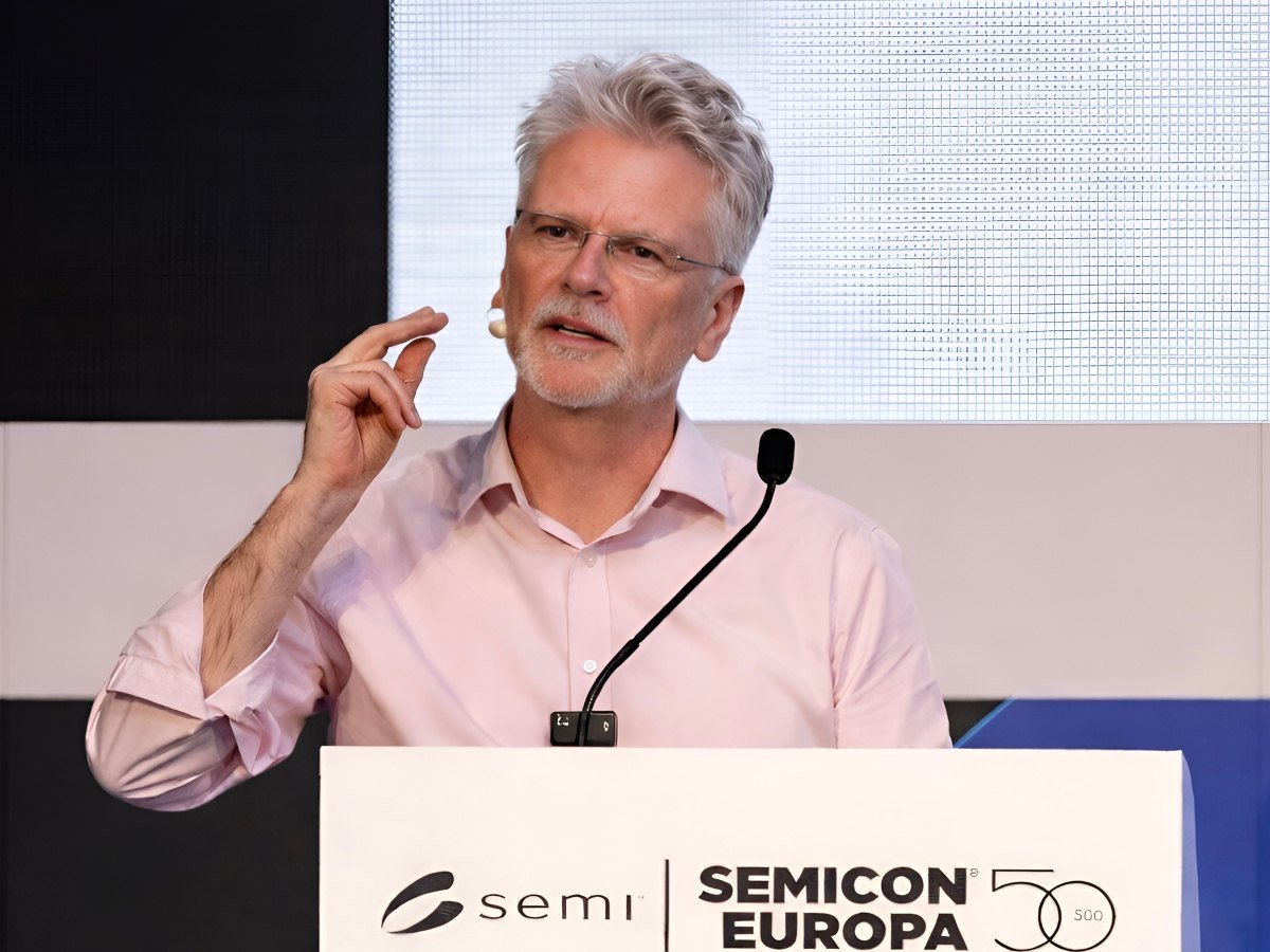 A man in a light pink shirt on a podium with a mic in front of him, talking.