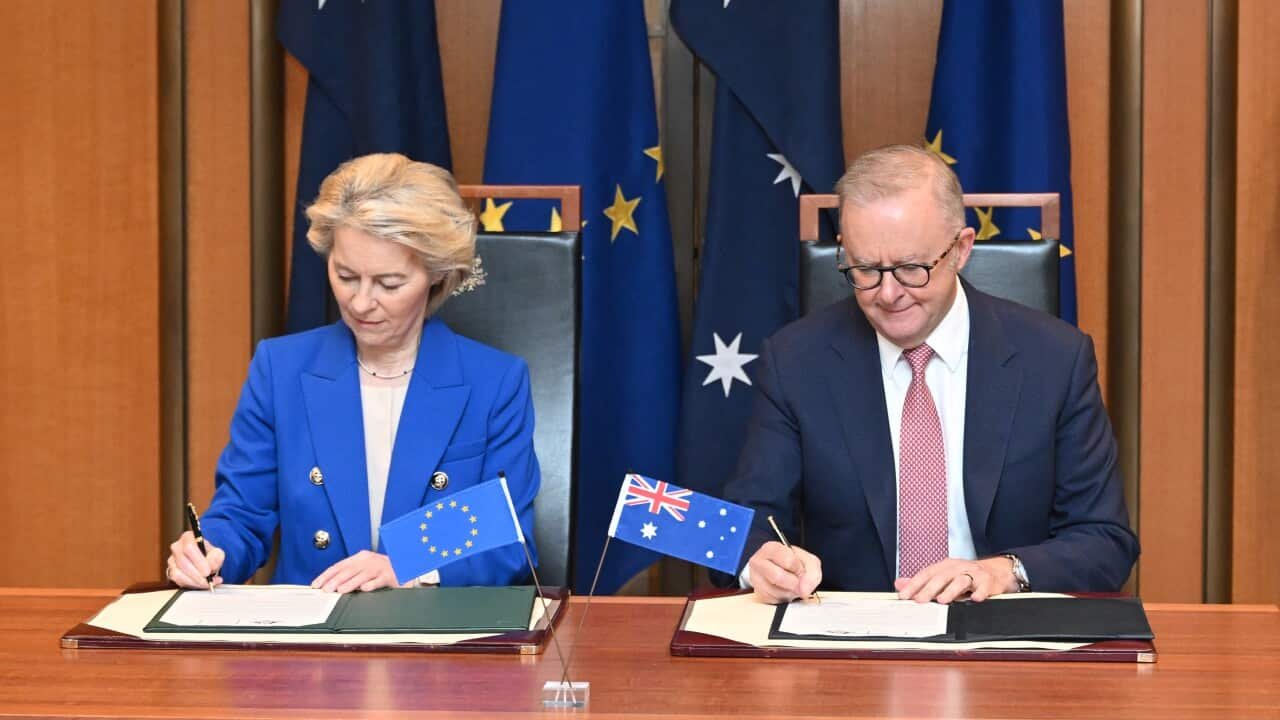 Ursula von der Leyen and Anthony Albanese sitting next to each other at a desk, signing documents. There are Australian and EU flags behind them.