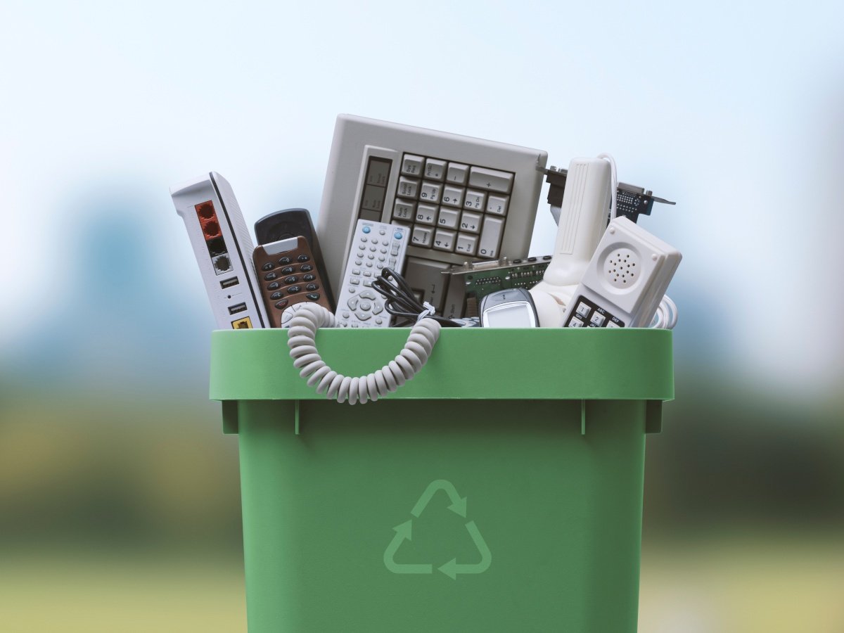 A green bin with old electronics overfilling the bin.