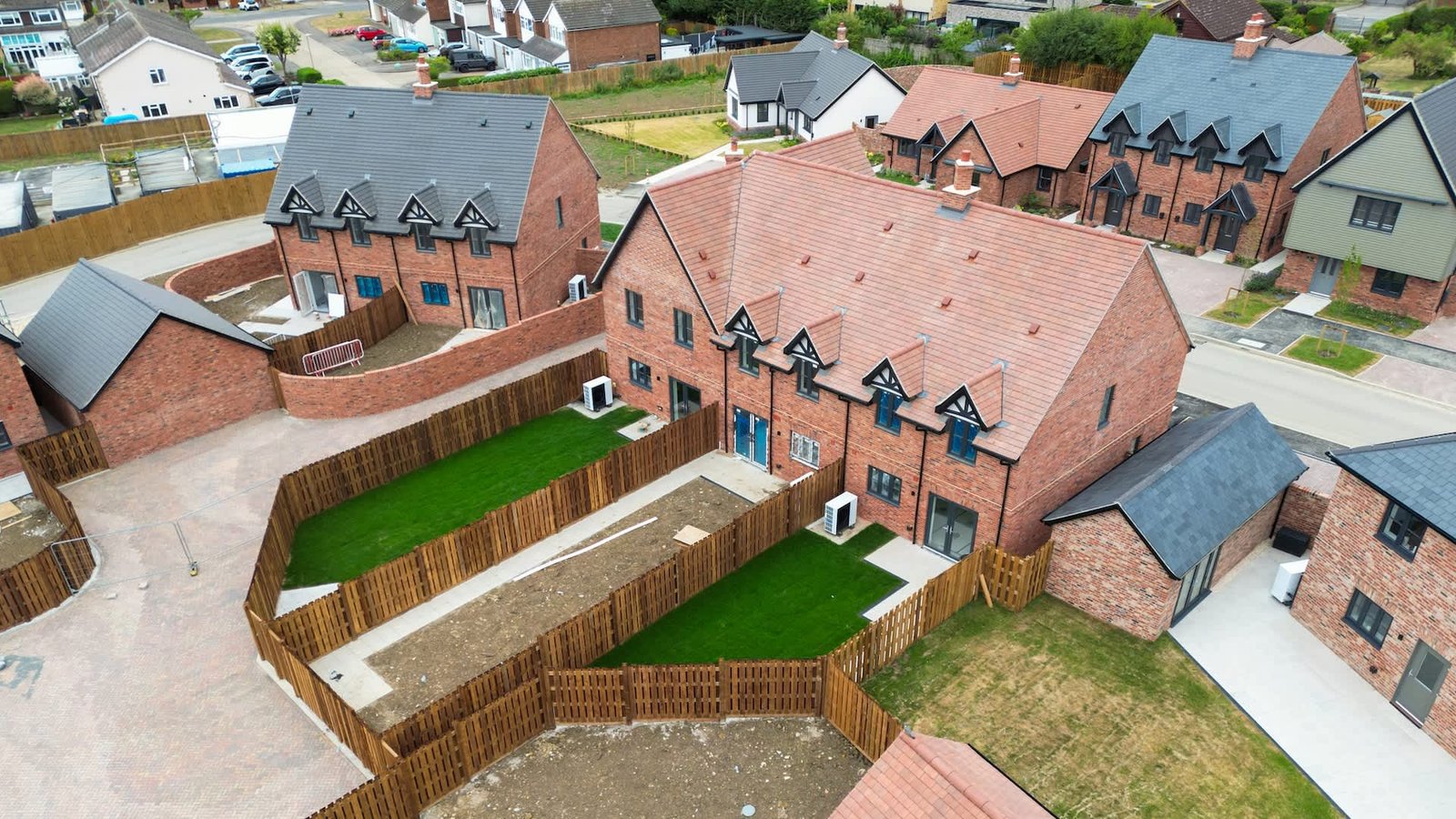 An aerial view of new brick houses with green lawns and wooden fences in a residential area.