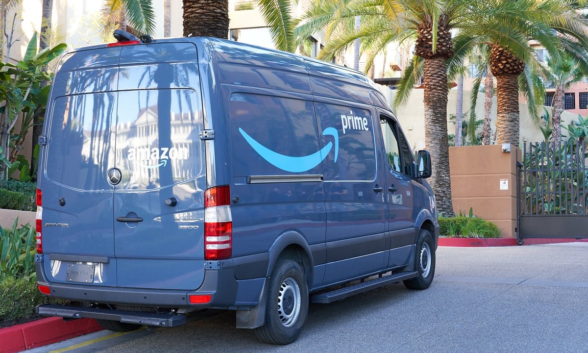 A parked, shiny blue Amazon van facing palm trees in front of a residential building.