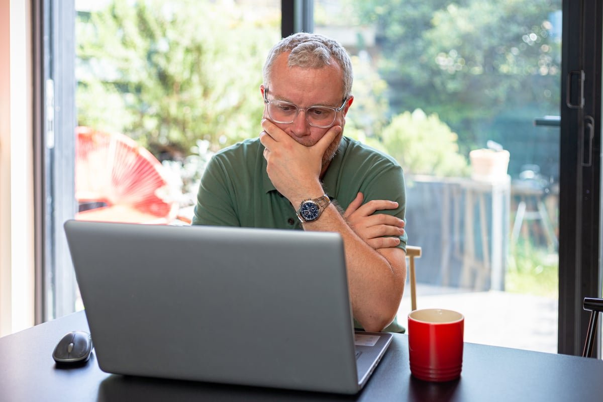 A person looks at a laptop with a worried expression on their face.
