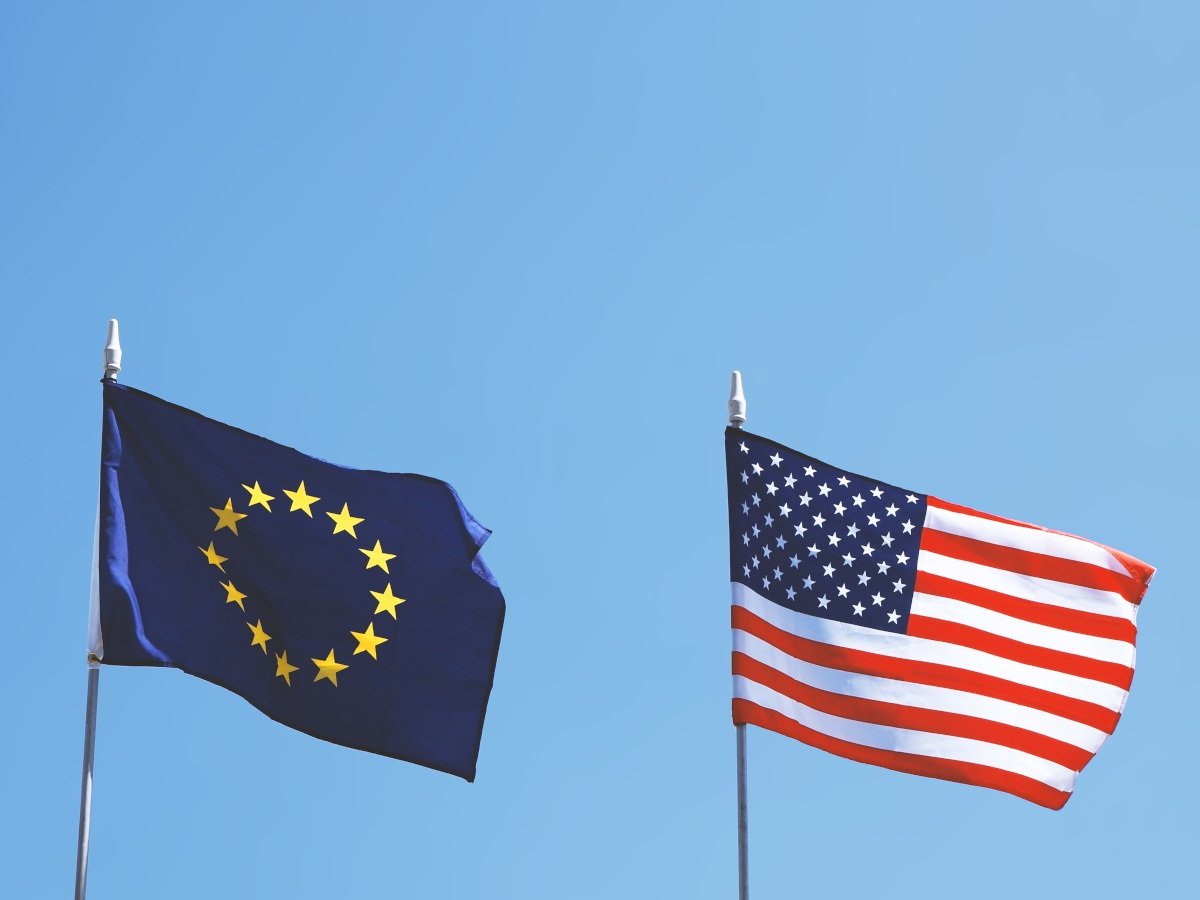 EU and USA flags on flag poles against a clear blue sky.