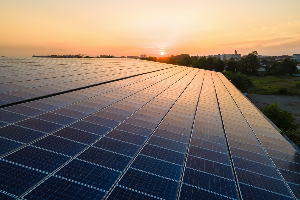 Blue photovoltaic solar panels mounted on building roof for producing clean ecological electricity at sunset. Production of renewable energy concept.
