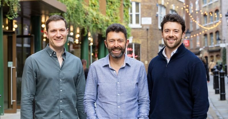 Three men stand outside smiling at the camera