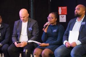 Ayanda Vabaza-Mvandaba sits alongside panelists at Startup Of The Year event speaking into the microphone.