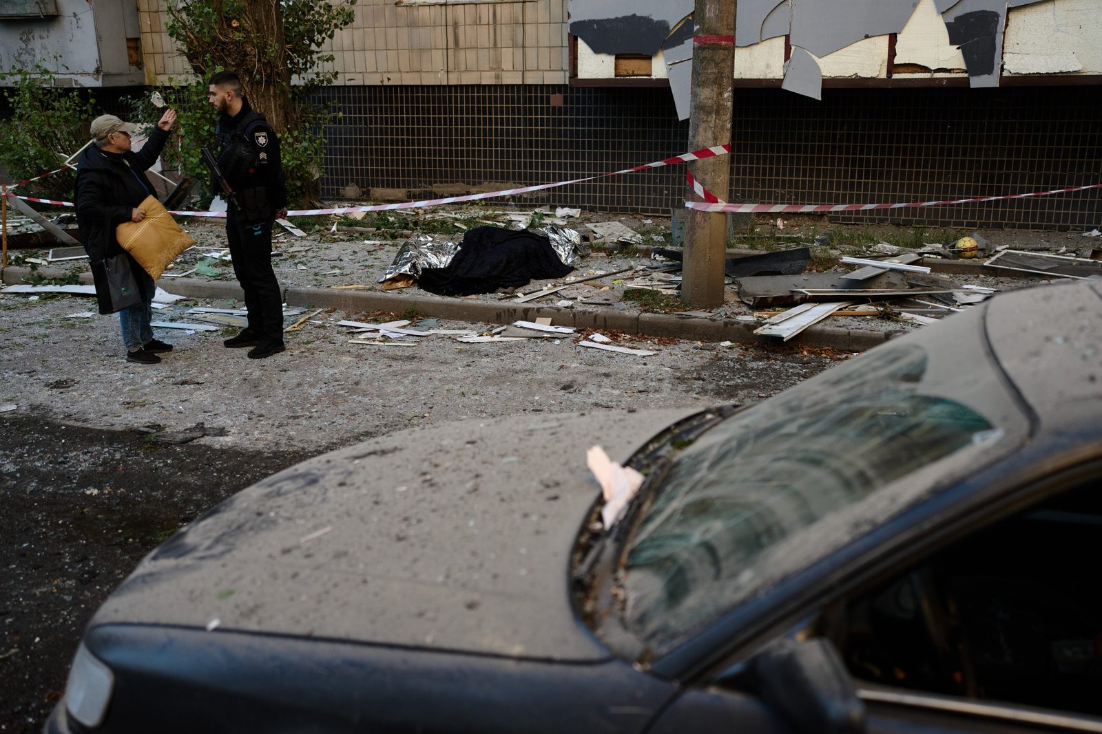A policeman talks to a local resident next to the bodies of two people killed during an overnight Russian attack in Kyiv, Ukraine, Thursday, Aug. 20, 2026. (AP Photo/Francisco Seco)