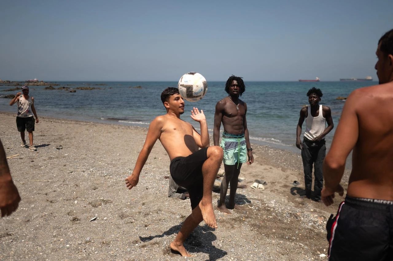 Migrants play with a ball as they wait to enter a short-stay migrants centre, CETI at Trampolin beach in Spain