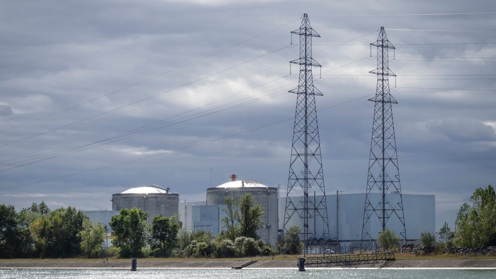 A nuclear power plant with cooling towers and high-voltage transmission lines under a cloudy sky.